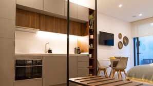 Een moderne keuken met een inbouwoven, een zithoek met tafel en stoelen, en een bed met uitzicht.