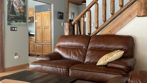 Ein Wohnzimmer mit einem braunen Ledersofa, einer Holztreppe und einer Küche im Hintergrund.