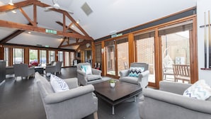 A spacious indoor area with grey sofas and a central coffee table, large windows with a view of a brick building, and wooden beams on the ceiling. - Charming 20-bed Self Contained Dwelling in Hook (Hook)