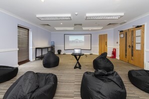 Ein Konferenzraum mit Projektorleinwand, schwarzen Sitzsäcken, einem kleinen Tisch und einem Wasserspender.