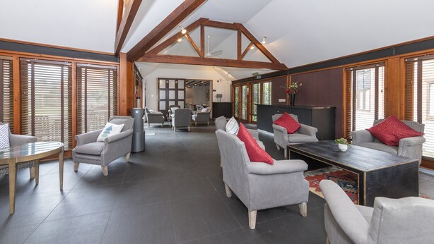 A spacious living area with high ceilings and exposed wooden beams, furnished with grey sofas and armchairs, and a central coffee table. - Charming 20-bed Self Contained Dwelling in Hook (Hook)