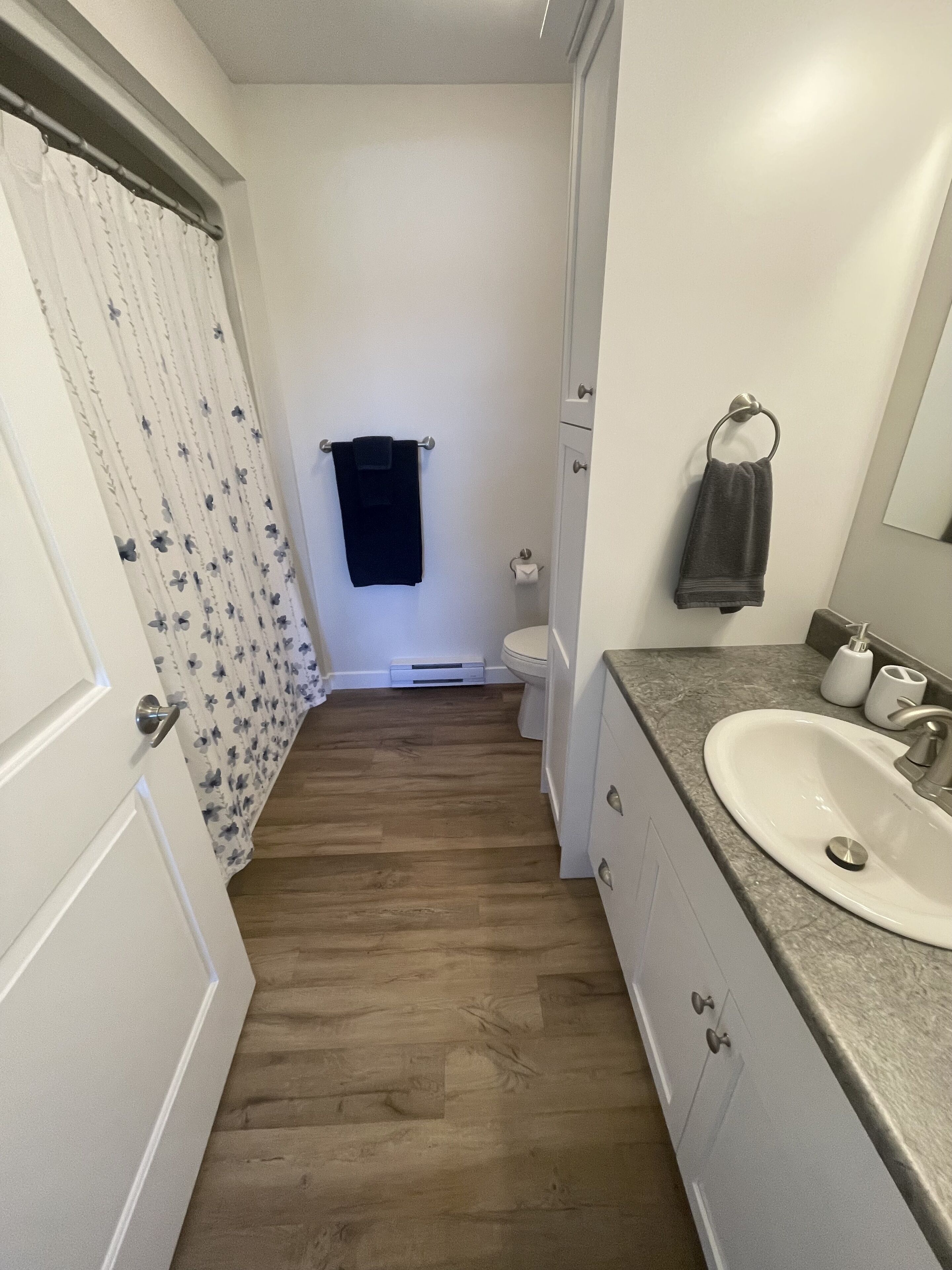 Ein Badezimmer mit Holzboden, weißen Wänden, einem weißen Waschbecken und einer Toilette.