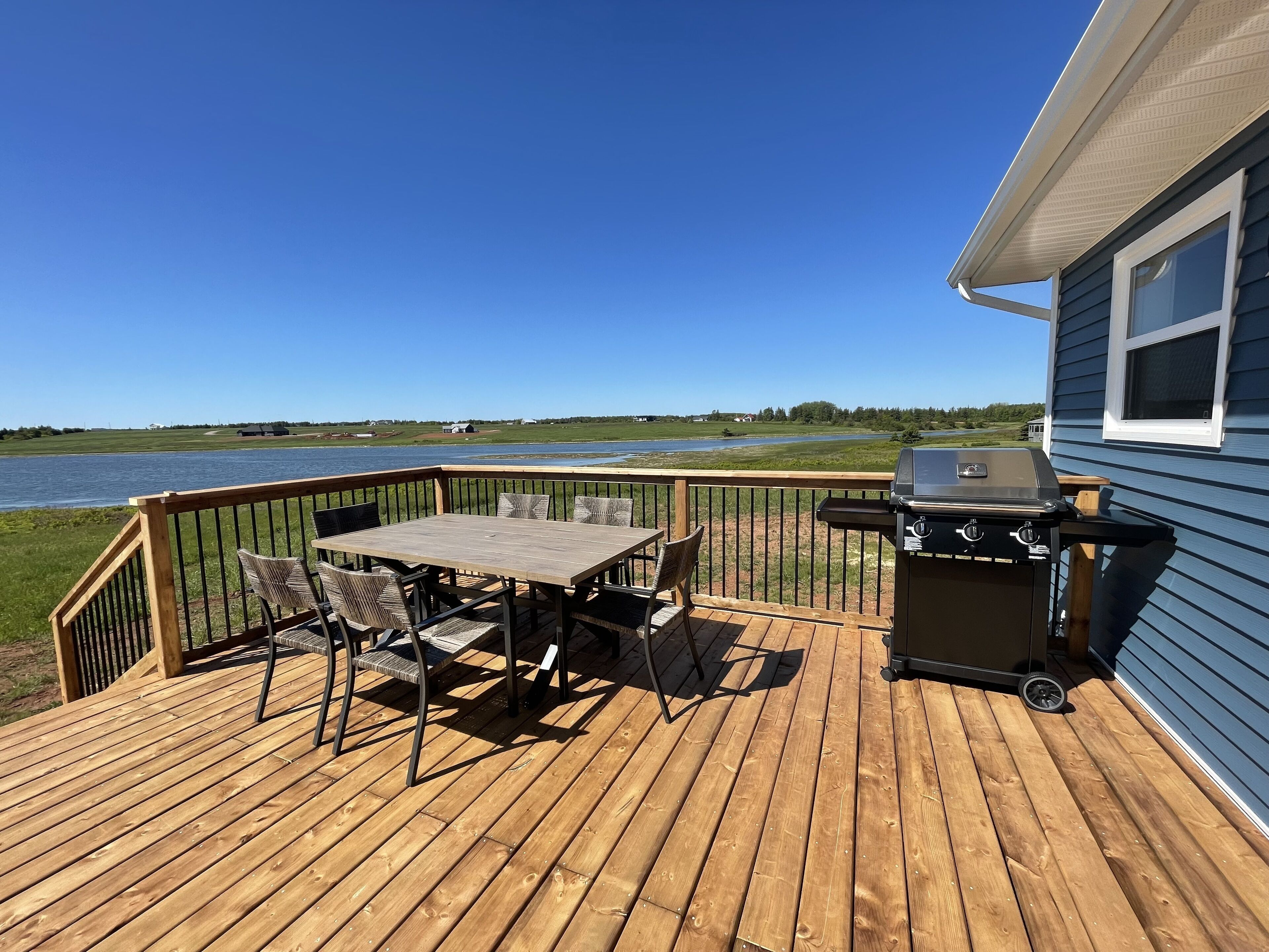Une terrasse en bois avec une table et des chaises, un barbecue et une vue sur un lac.