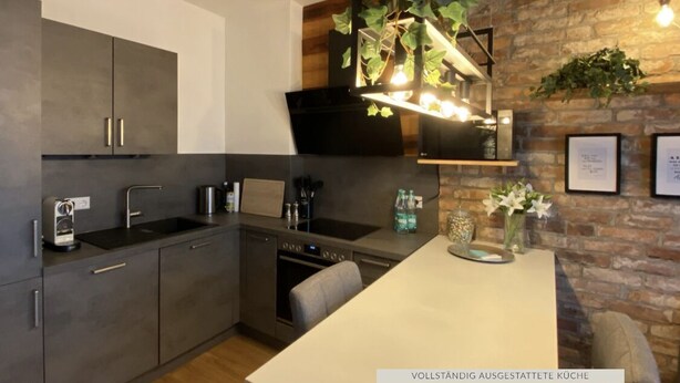 A modern kitchen with grey cabinets, a built-in oven, and a hanging light fixture with plants.