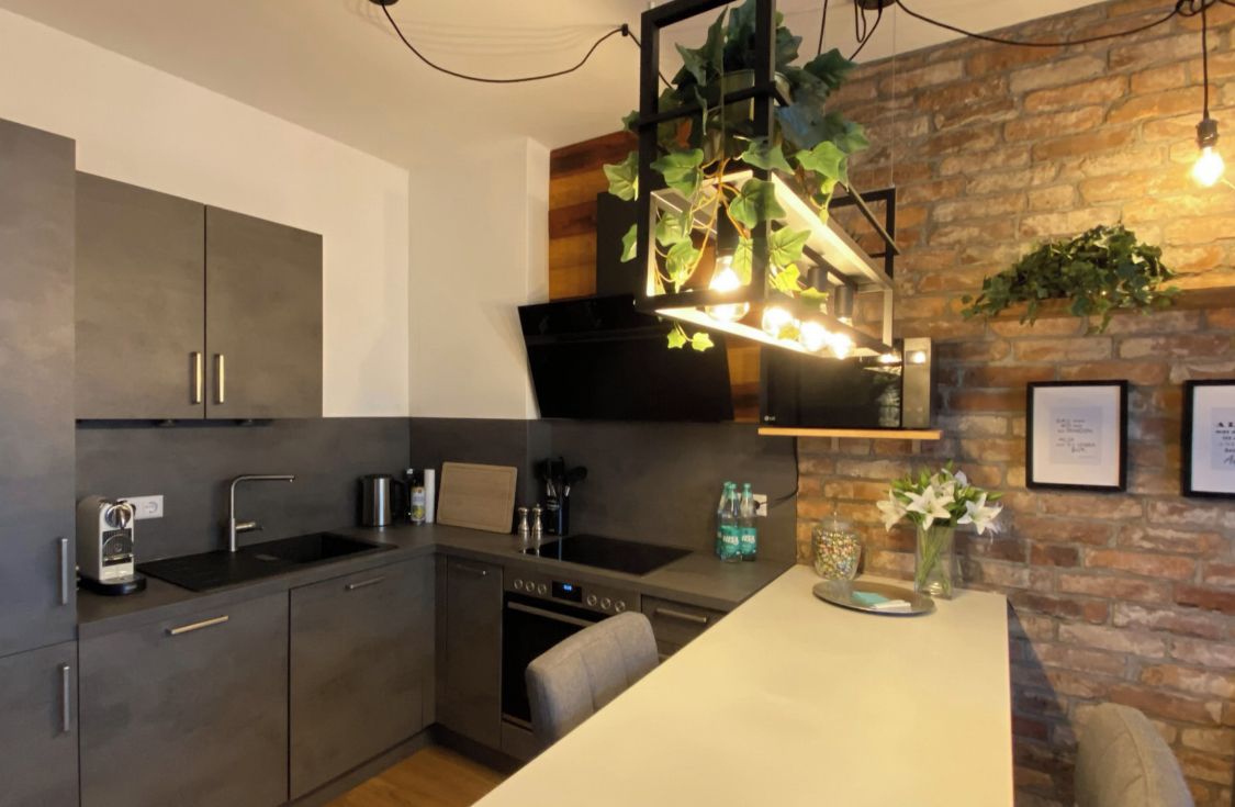 A modern kitchen with grey cabinets, a built-in oven, and a hanging light fixture with plants.