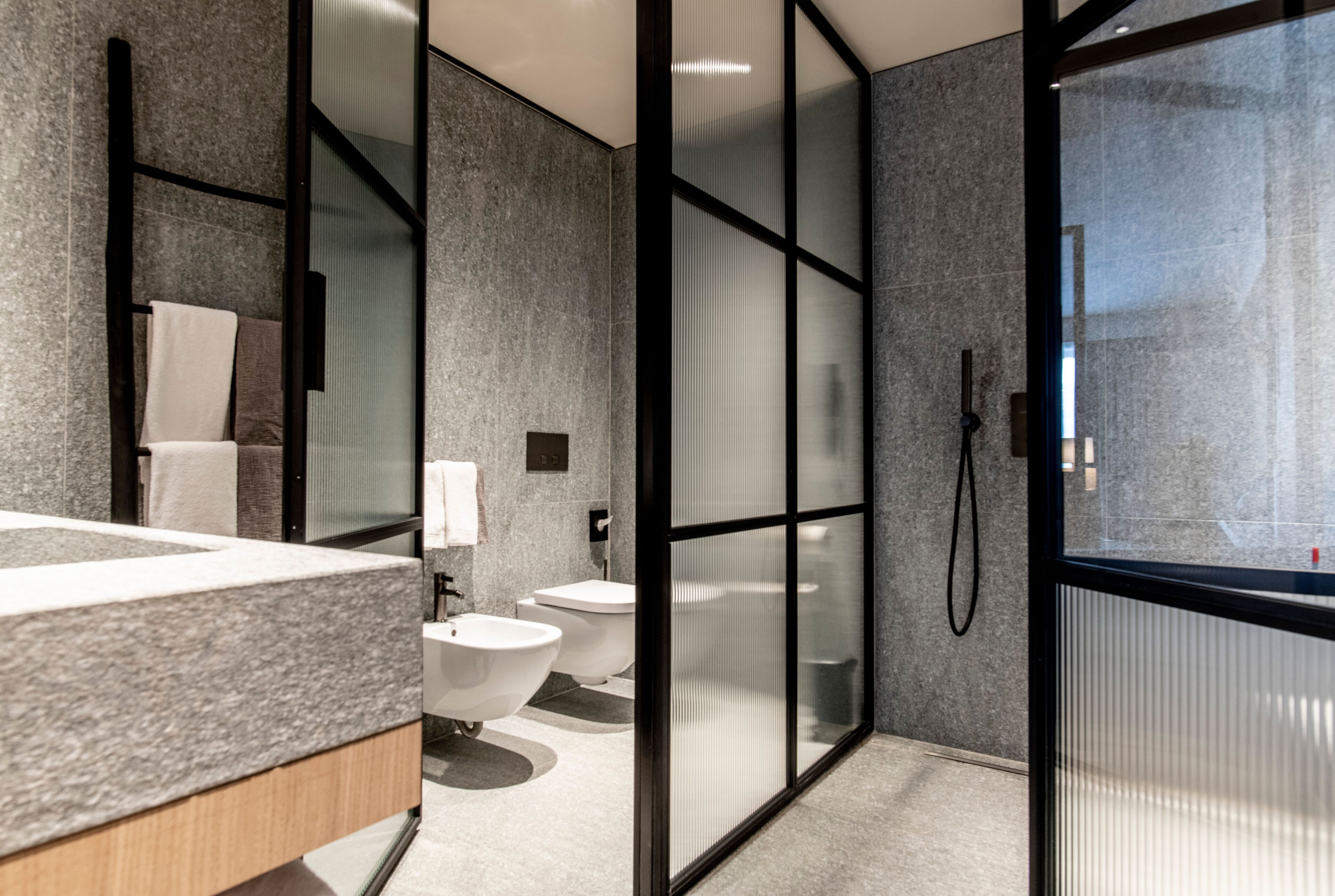 A modern bathroom with a granite countertop, a freestanding bathtub, a toilet, and a glass-enclosed shower area.