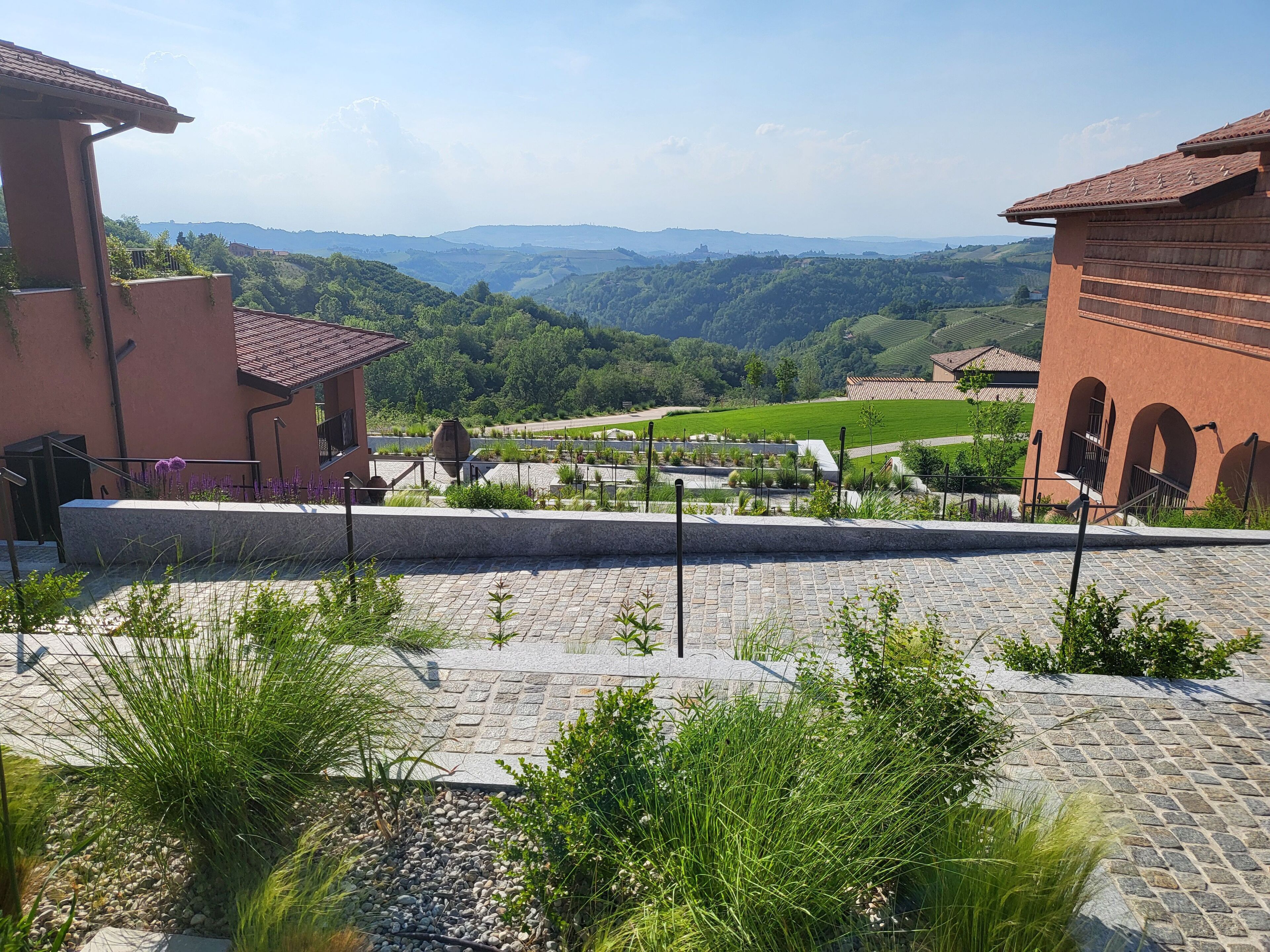 A courtyard with stone paving, a view of green hills, and traditional architecture.