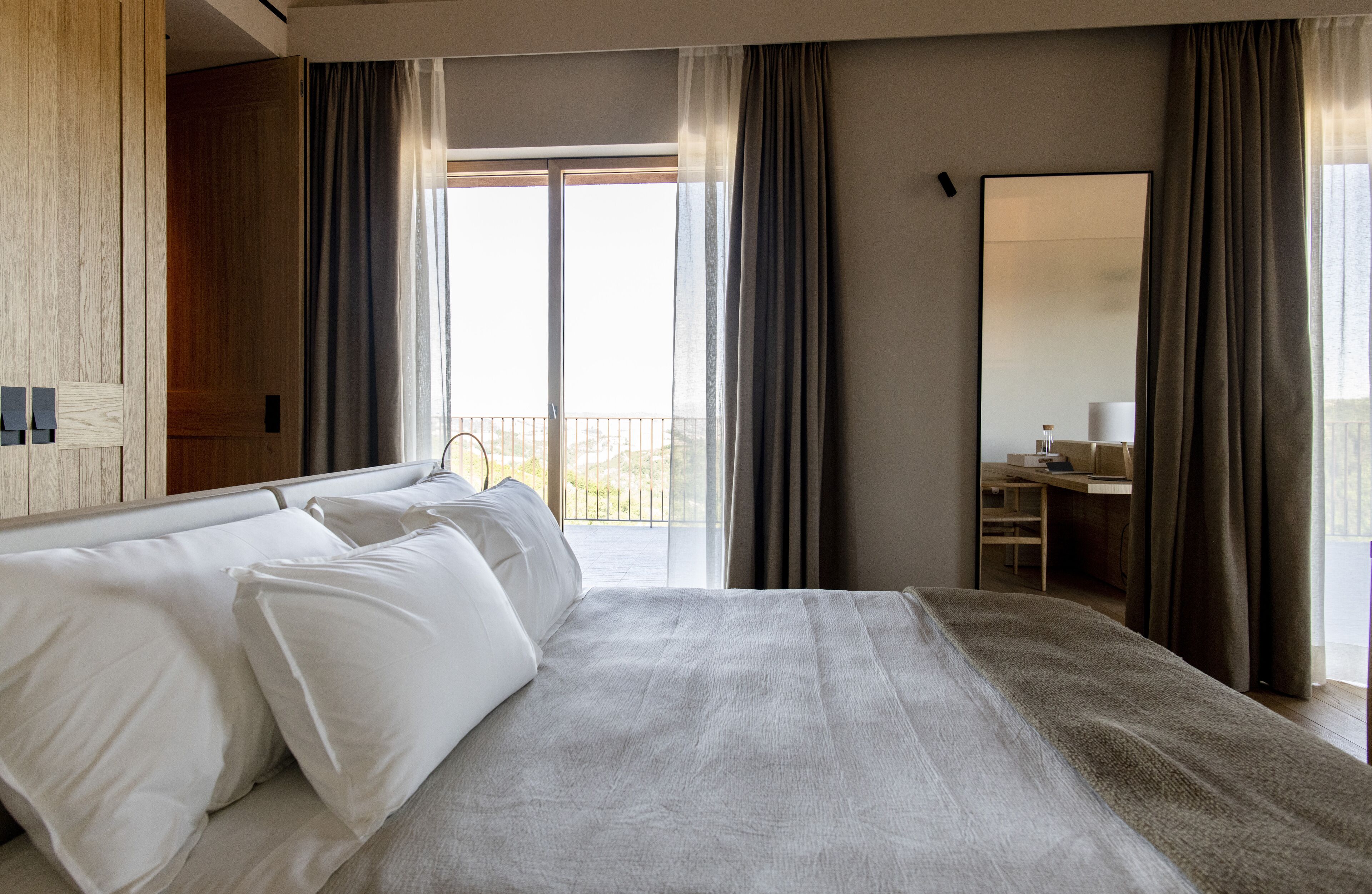 A modern hotel room with a large bed, a desk, and a balcony with curtains.