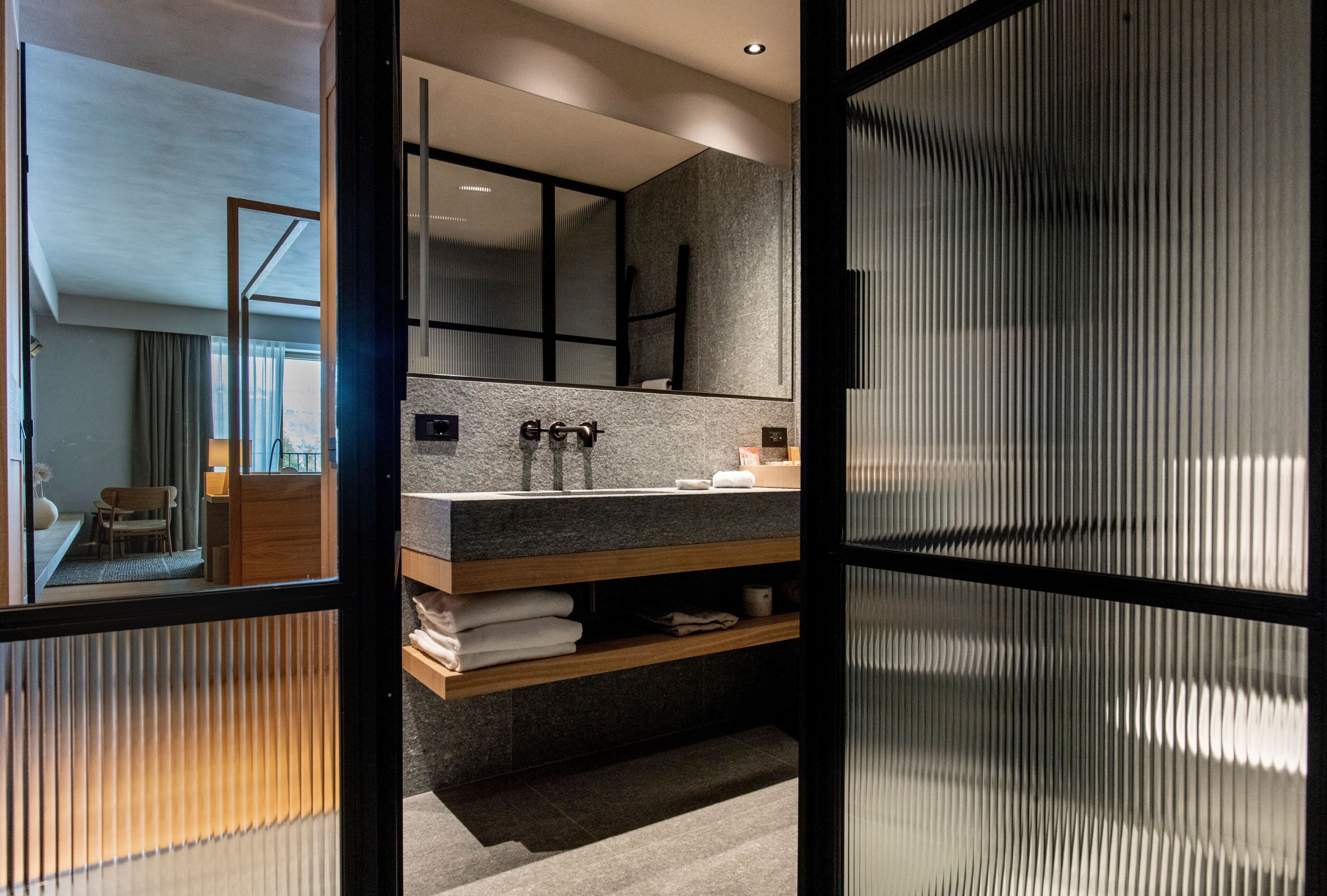 Un baño moderno con un espejo grande, encimera de granito y estante de madera.