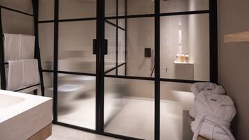 A modern bathroom with a glass partition, a sink, and a robe hanging on a rack.