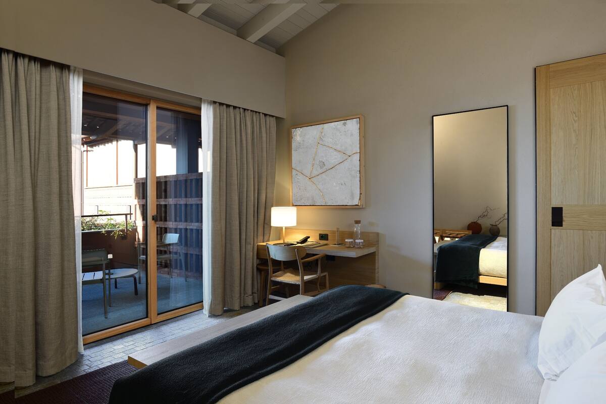 Une chambre d’hôtel avec un lit, un bureau, une chaise, une lampe et un grand miroir.