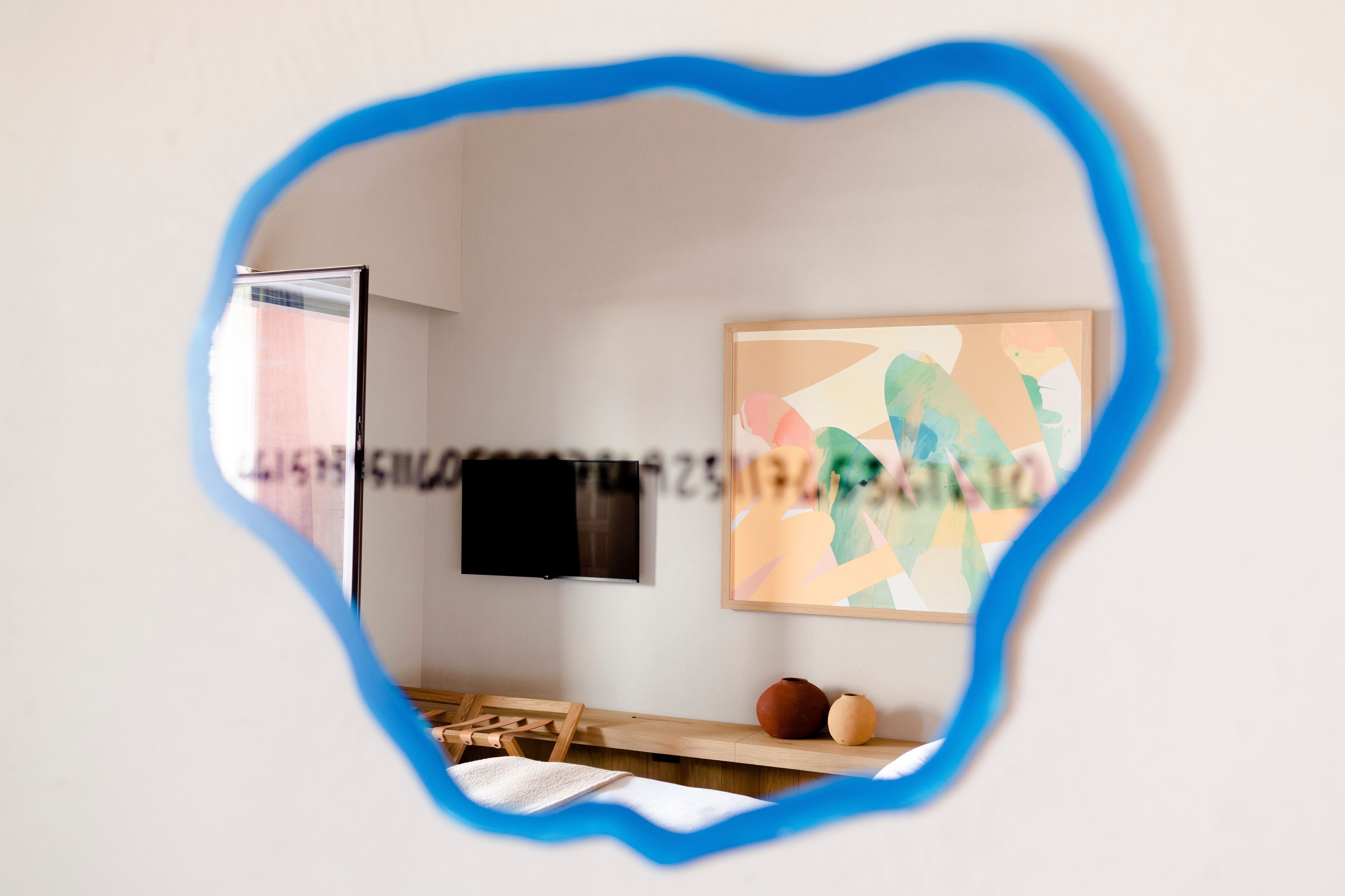 A room with a flat-screen TV mounted on the wall, a wooden desk, and a framed abstract painting.