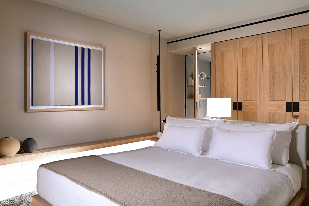 Une chambre d’hôtel moderne avec un grand lit, une table de chevet, un miroir et une armoire en bois.