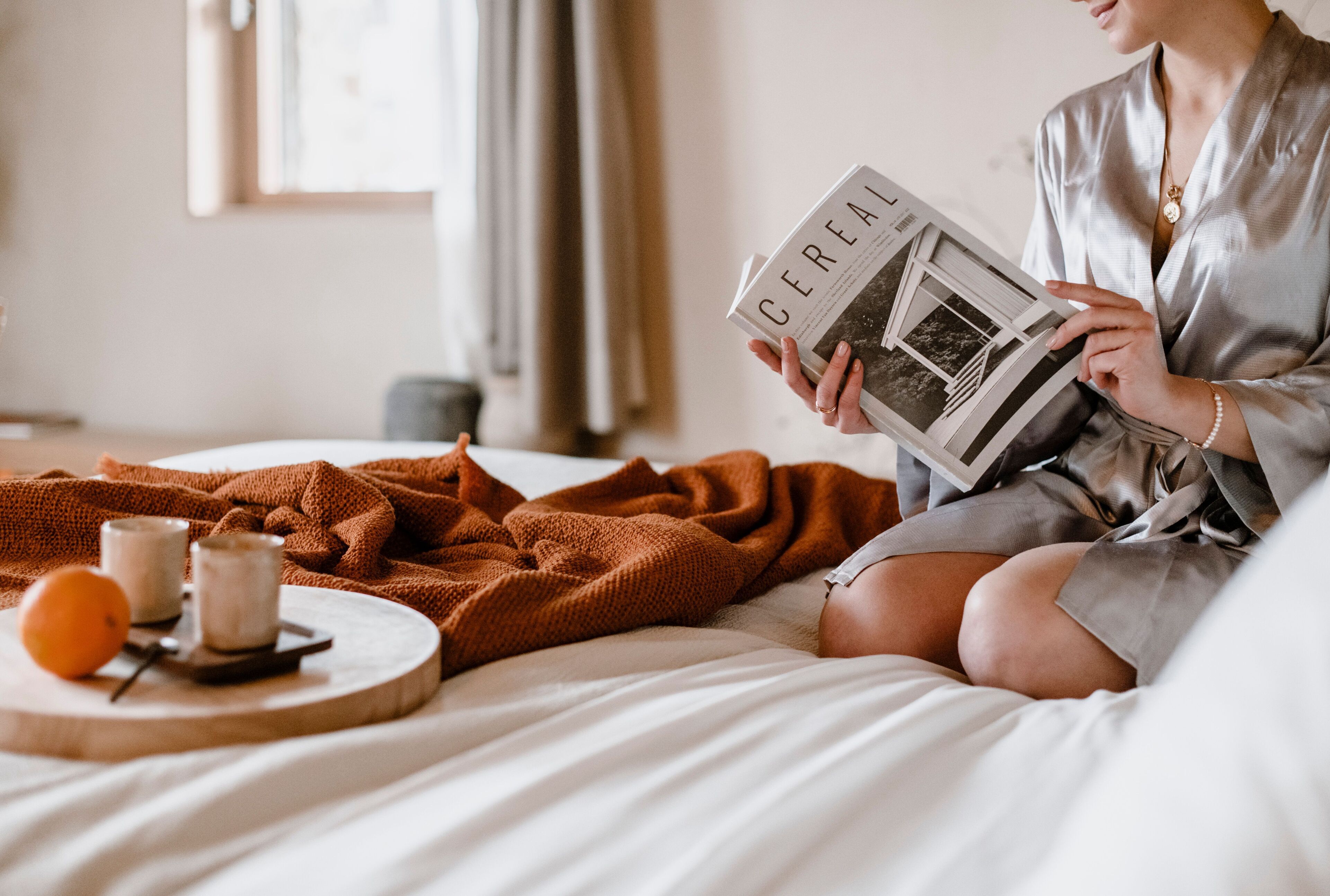 A person sitting on a bed reading a book titled 'Cereal'.