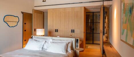 A modern bedroom with a large bed, wooden wardrobe, bedside tables, and a bathroom visible through an open door.