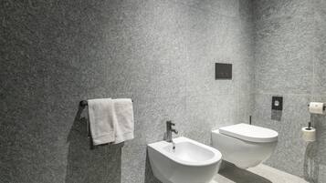 Et moderne badeværelse med bidét, toilet og håndklæderække foran en væg med struktur.