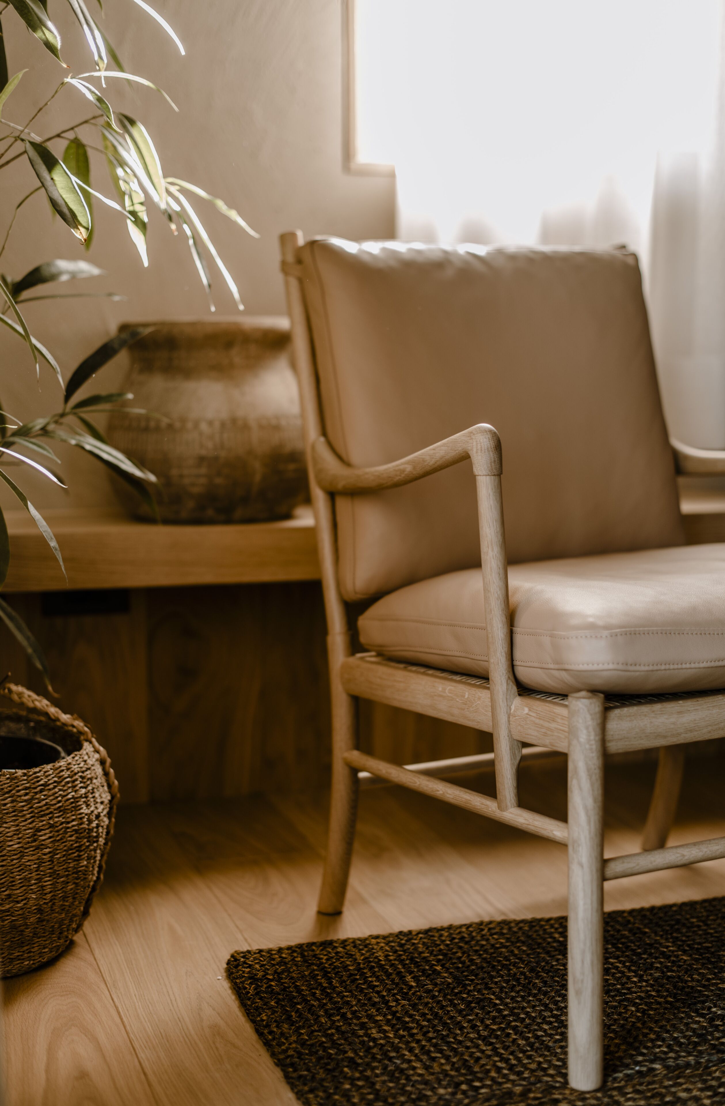 Una silla de madera con cojín, una cesta trenzada y una planta en maceta sobre un piso de madera.
