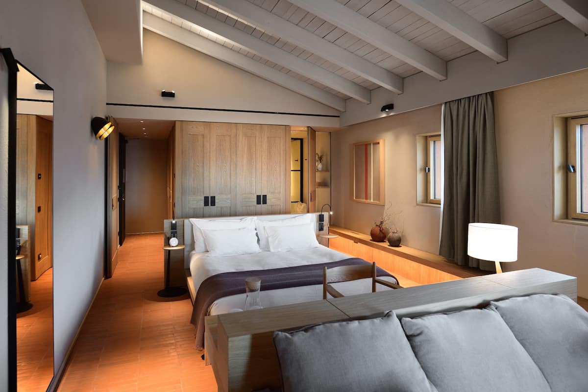 Une chambre d’hôtel moderne, dotée d’un grand lit, de tables de chevet, d’un bureau et donnant sur le couloir.