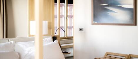 A hotel room with a bed, a window, a painting, and a radiator.