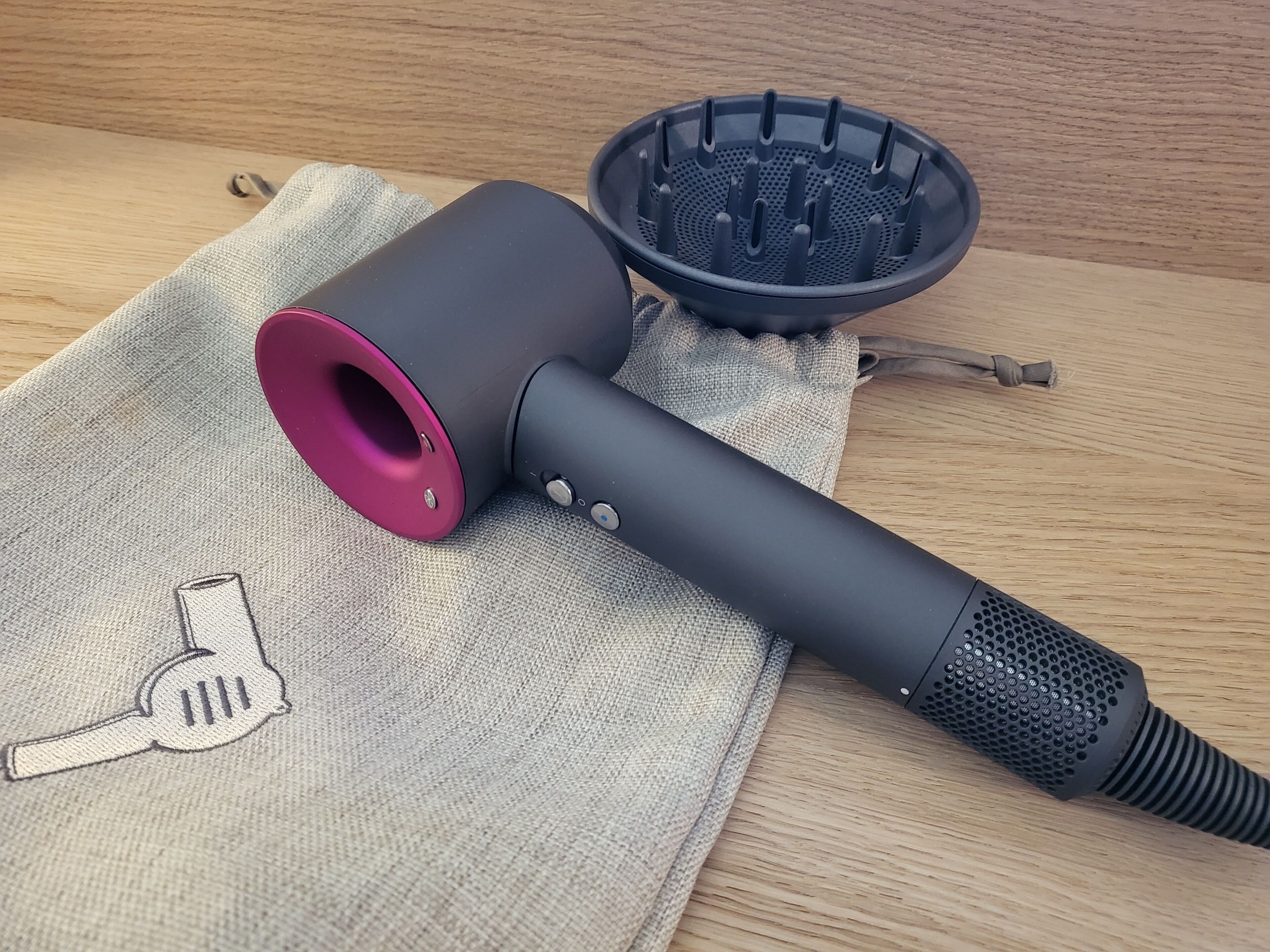 A hairdryer with a red nozzle and a black diffuser on a beige cloth.