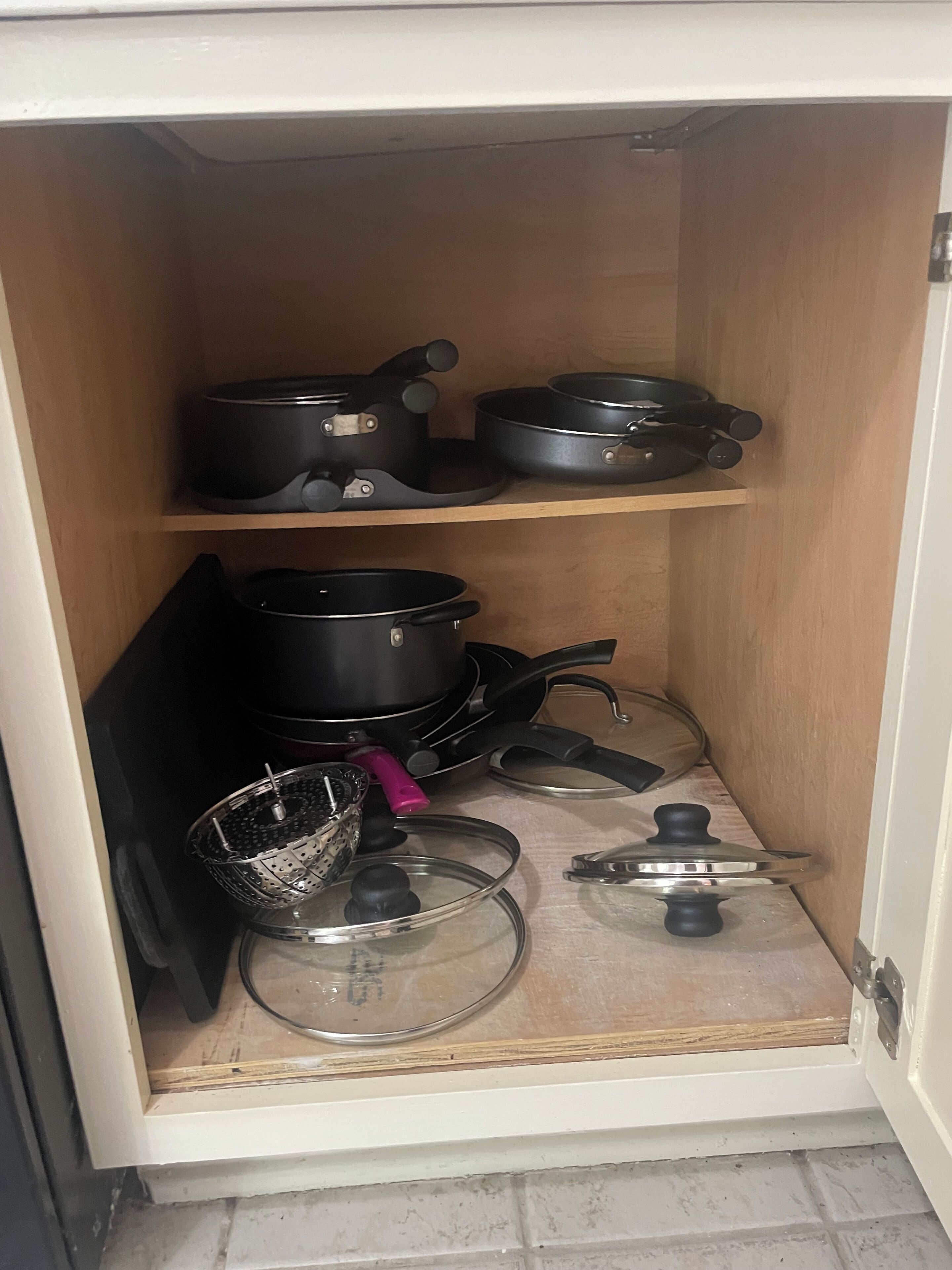 Un pensile da cucina con pentole e padelle nere, e un colino in metallo.