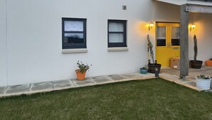 Een modern gebouw met een witte gevel, twee ramen, een gele deur en buitenverlichting.