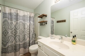 A bathroom with a shower curtain, toilet, sink, and mirror. - Relax in a Spacious 3 Bedroom + Office- Mud Island/Downtown  (Memphis)