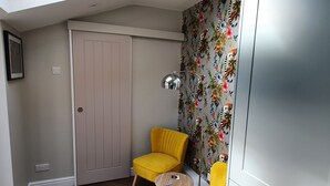 A room with a sliding door, a yellow chair, a small round table, and a wall with a floral wallpaper. - Millside (Lincoln)