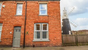 A red brick house with two windows, a door, and a windmill in the background. - Millside (Lincoln)