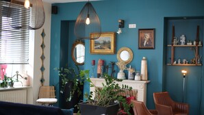 Sala de estar com lareira, várias poltronas, uma planta em vaso grande e objetos decorativos nas prateleiras.