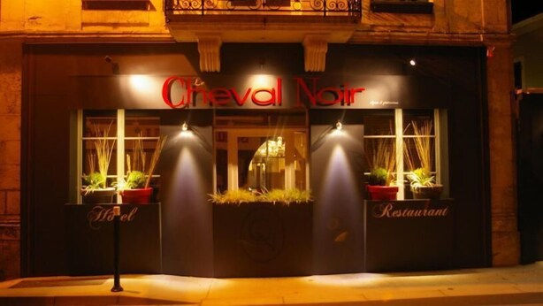 Exterior do restaurante Creval Noir, com letreiros iluminados e plantas em vasos na entrada.