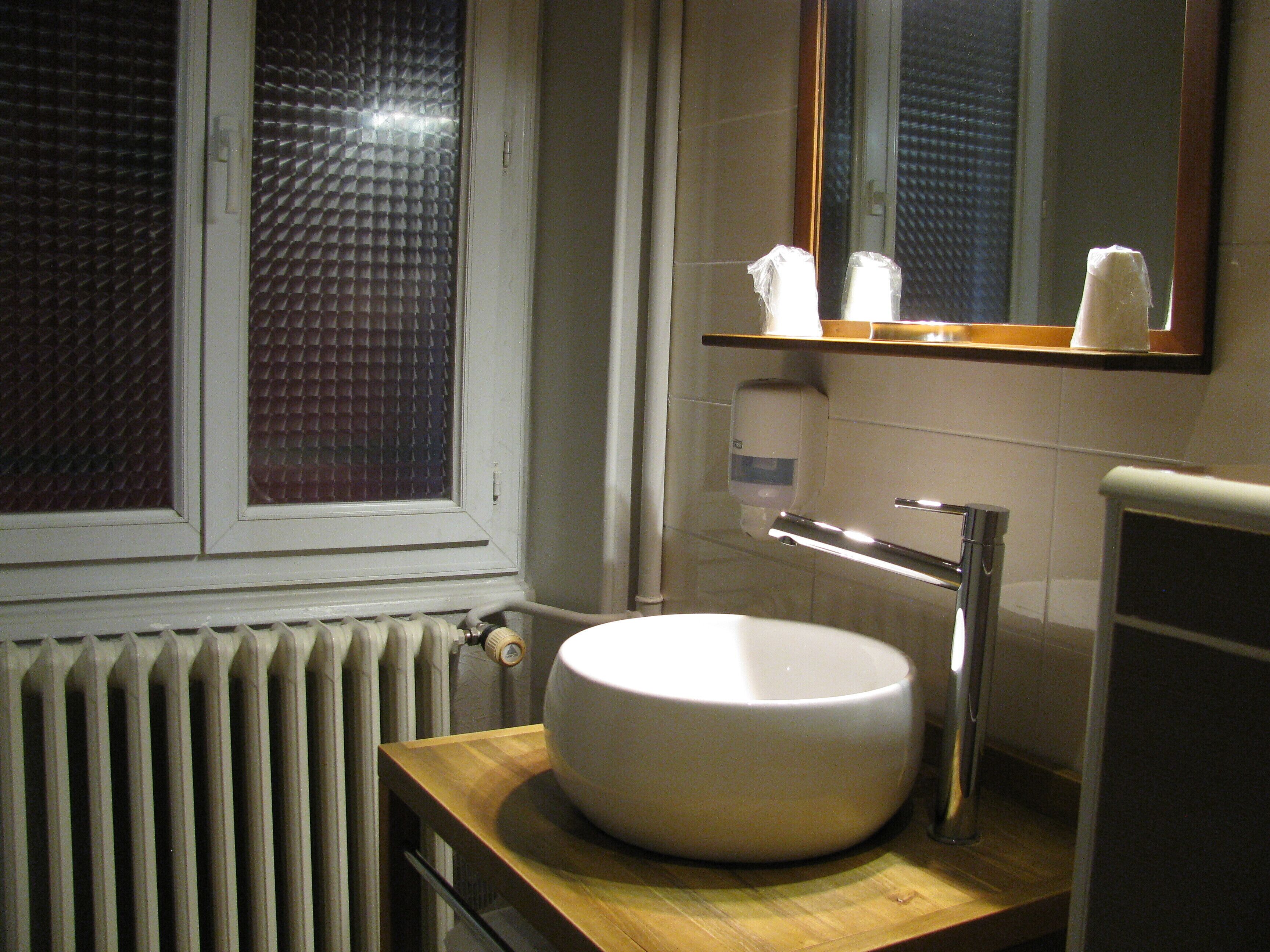 Un baño con lavamanos redondo, un espejo y una ventana con persianas.