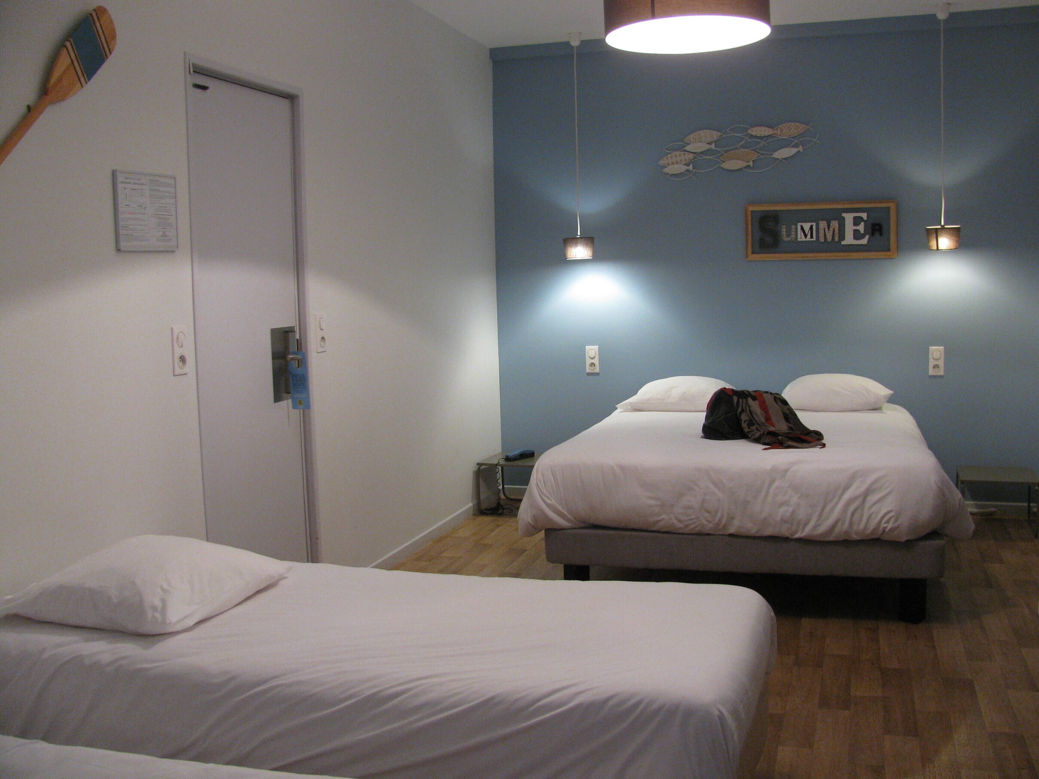 A hotel room with two beds, a wooden paddle on the wall, and a 'SUMMER' sign.