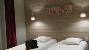 Quarto de hotel com duas camas de solteiro, paredes com painéis de madeira e cortina vermelha.