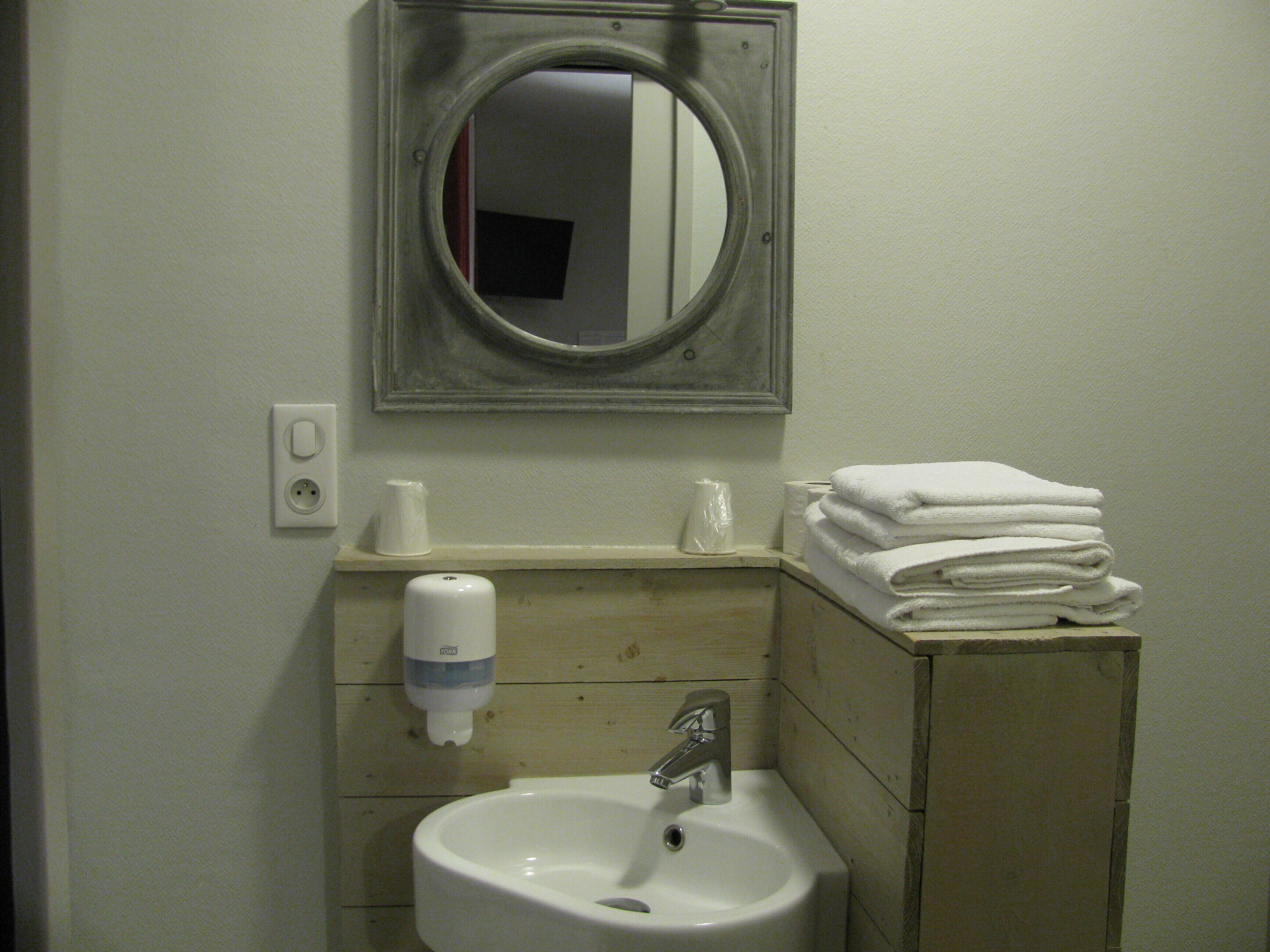 A bathroom with a sink, mirror, towel stack, soap dispenser, and toilet paper.