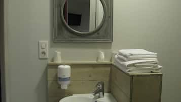 A bathroom with a sink, mirror, towel stack, soap dispenser, and toilet paper.