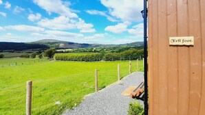 Ein Holzhaus mit einem Schild, auf dem 'Fell foot' steht, in ländlicher Umgebung mit blauem Himmel und grünen Feldern.