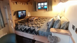 Ein gemütliches Wohnmobil-Interieur mit einem Bett, einem Fernseher und einem kleinen Fenster mit Vorhängen.