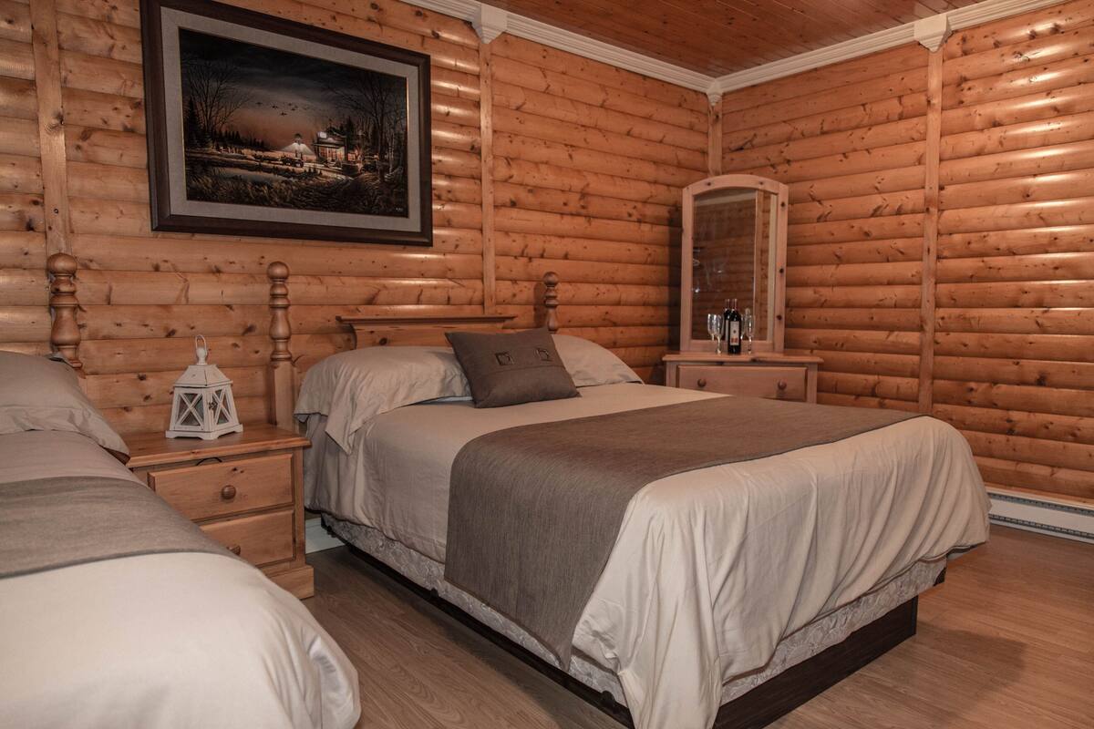 Een slaapkamer in blokhutstijl met twee bedden, een nachtkastje met een lantaarn, een spiegel en een lijst met een afbeelding aan de muur.