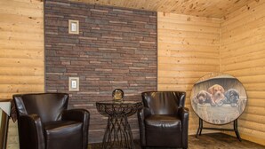 A cozy room with wooden walls, two leather armchairs, a small table with a decorative item, and a round table with a dog print. - Viking Lodge Motel (Pistolet Bay)
