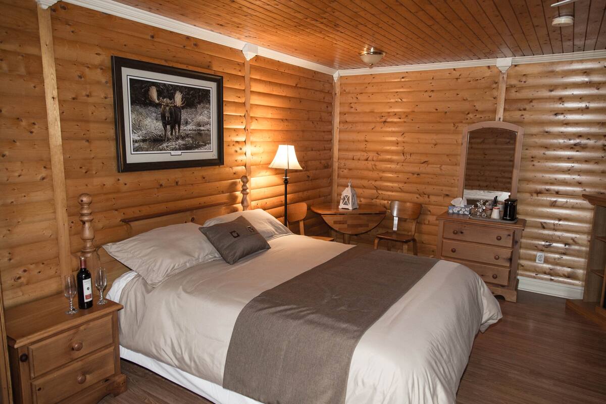 Een slaapkamer in blokhutstijl met een bed, nachtkastjes, een lamp, een klein tafeltje en een kapstok.