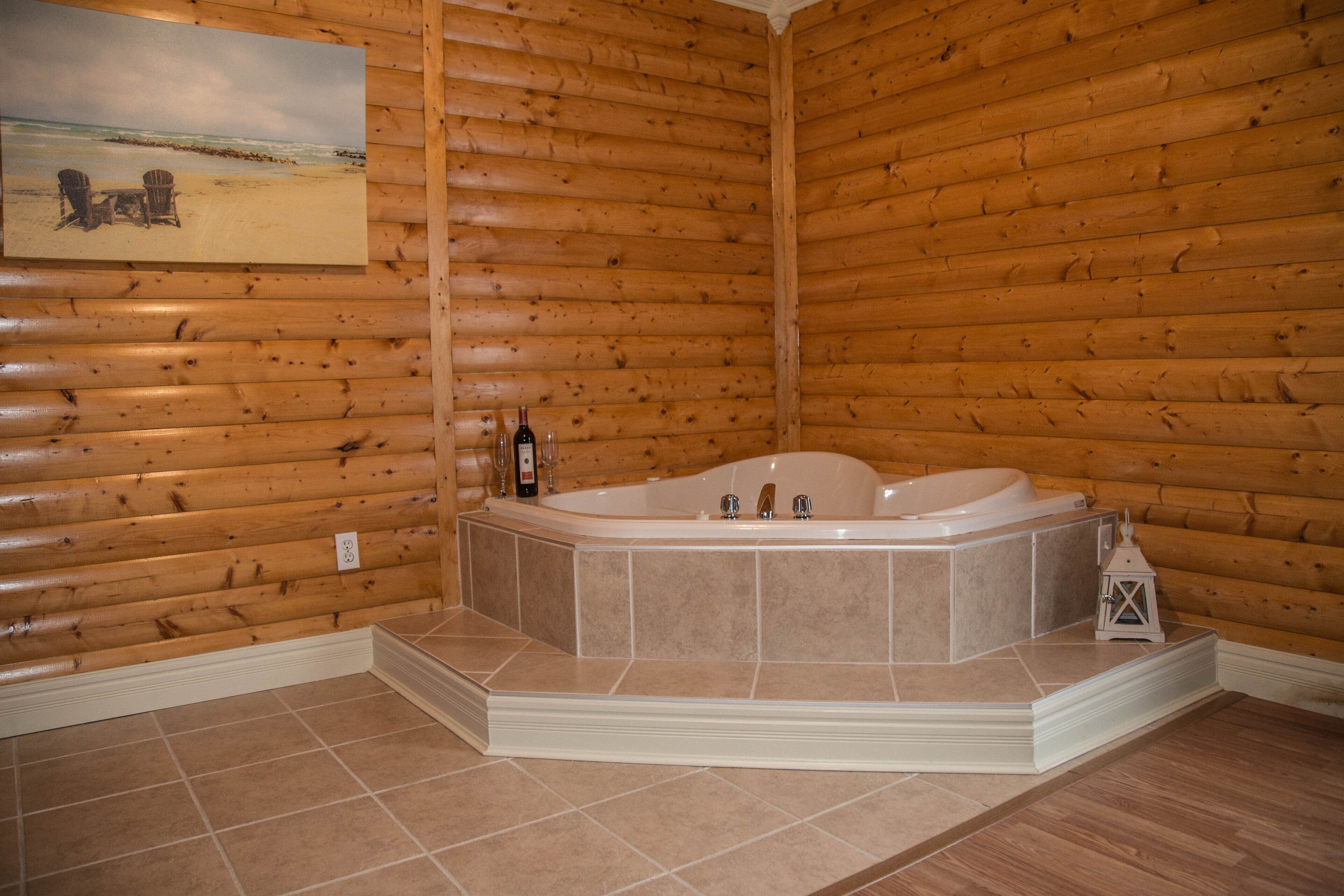 Une salle de bain rustique, aménagée dans une cabane en rondins, avec une grande baignoire, des murs en bois et un tableau représentant une scène de plage.