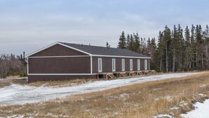 A large, single-story building with a brown exterior and white trim, featuring a covered outdoor area with wooden benches. - Viking Lodge Motel (Pistolet Bay)