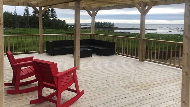 A covered deck with a wooden floor, red rocking chairs, and a black sectional sofa. - Viking Lodge Motel (Pistolet Bay)