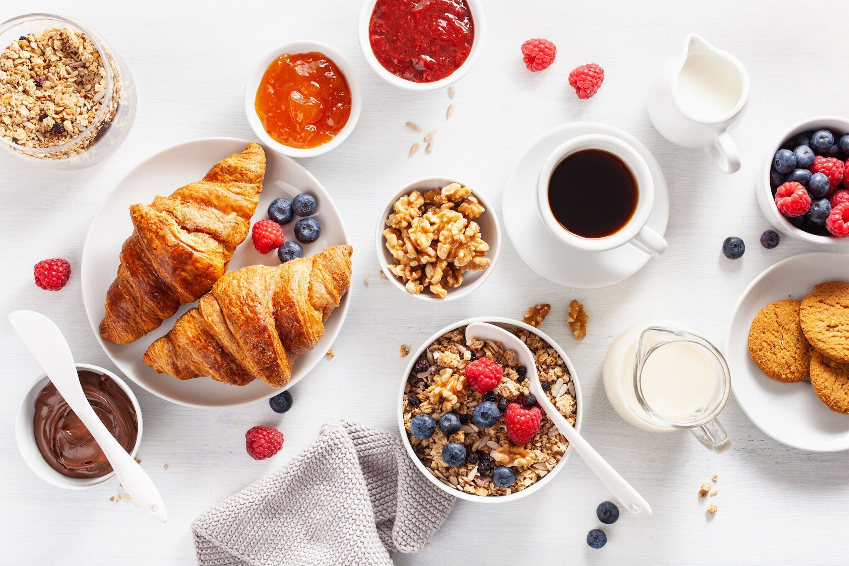A breakfast setting with croissants, berries, granola, and coffee.