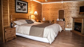 A log cabin-style bedroom with a wooden bed, bedside tables, a fireplace, and a mounted television. - Viking Lodge Motel (Pistolet Bay)