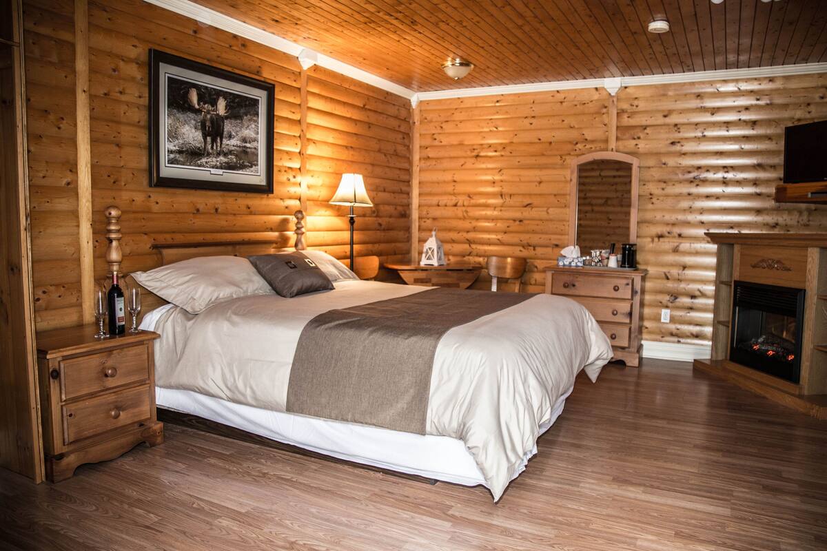 Een slaapkamer in blokhutstijl met een houten bed, nachtkastjes, een open haard en een bevestigde televisie.