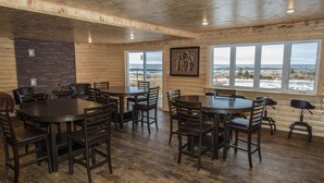 A spacious room with wooden walls and floors, featuring multiple round tables and chairs, large windows with a view of the beach, and a fireplace. - Viking Lodge Motel (Pistolet Bay)