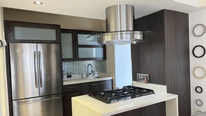 A modern kitchen with a stainless steel refrigerator, a gas stove, and dark wooden cabinets. - Beautiful home 10 min from everythin!! (luquillo)