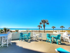 Relax on the beachside patio with ocean views, surrounded by palm trees and comfortable seating.